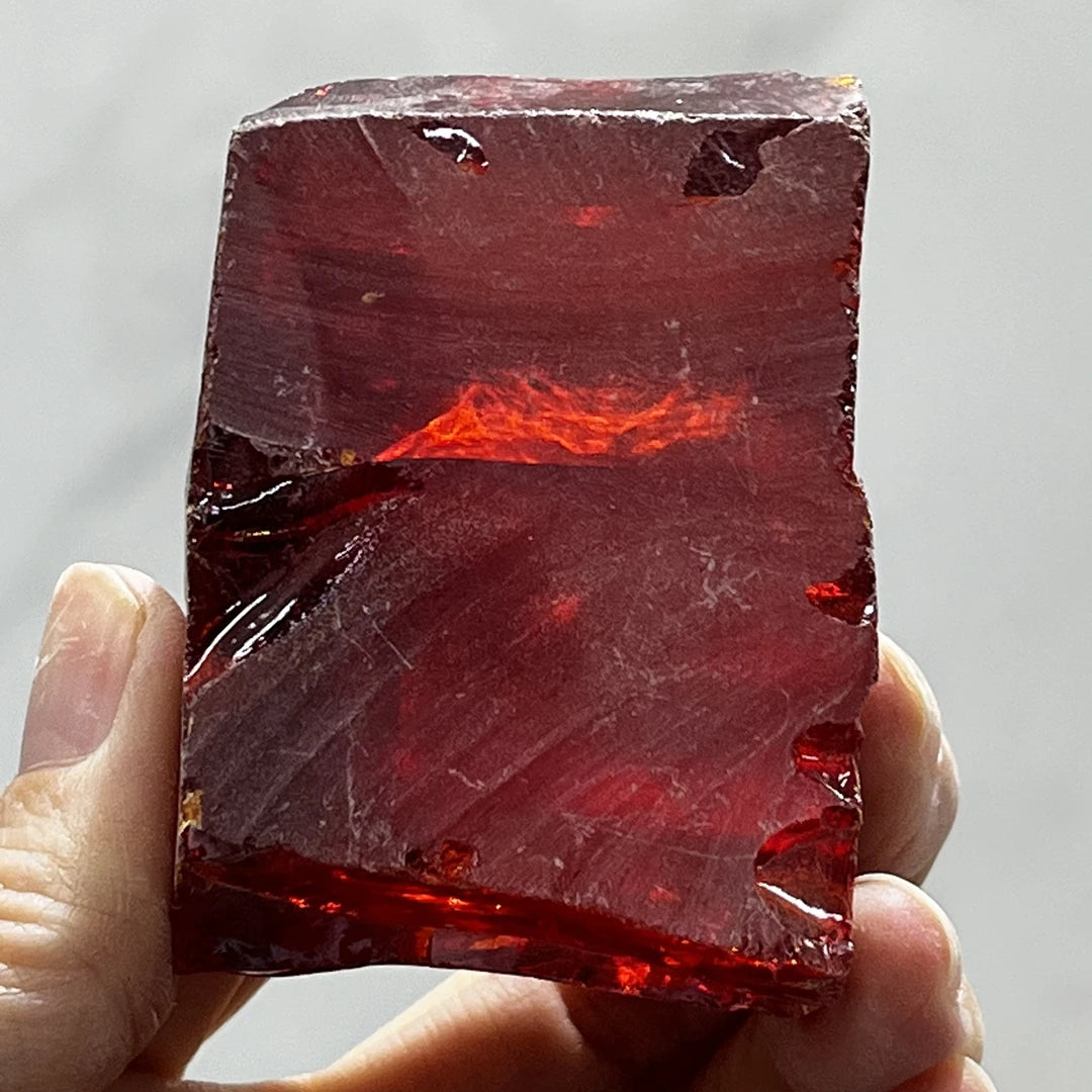 Loose red rough cubic zirconia slab, uncut faceted with glowing red highlight, held