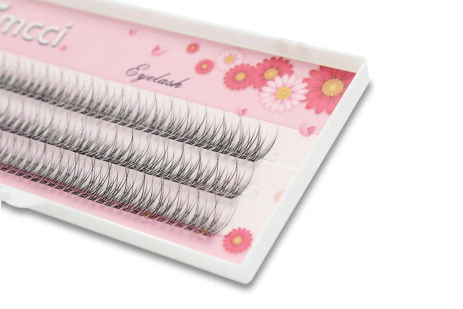 Black mink 3D cluster eyelash extensions arranged in rows on a white tray with pink floral background.