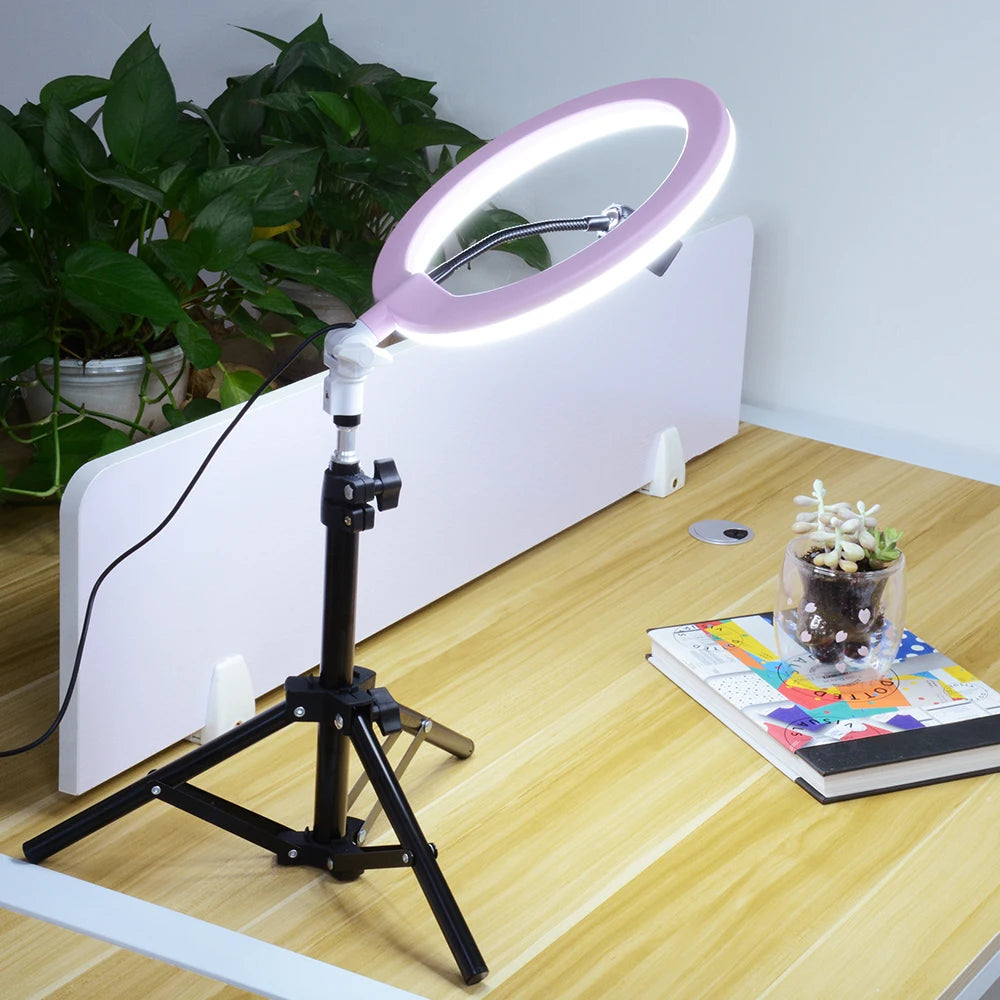Pink LED ring light on a black tripod stand, used for desktop photography and video lighting.