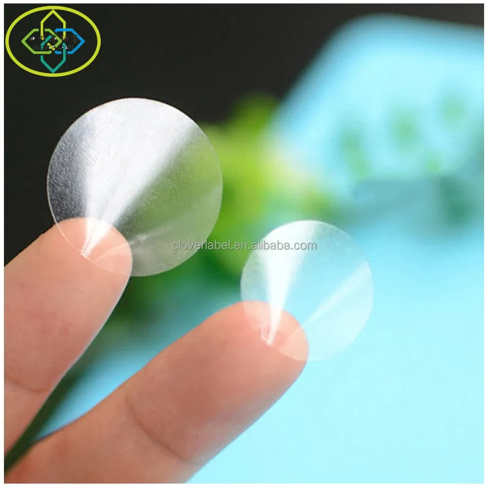 Clear round vinyl label sticker held on fingertip, see-through adhesive surface