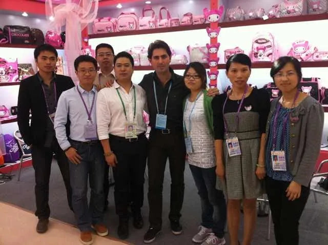 Group of business professionals standing in front of retail display shelves stocked with pink patterned trunks and bags.