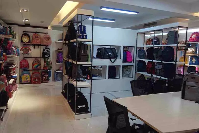 Showroom display of black travel trunks and assorted colorful school backpacks on tiered shelves.