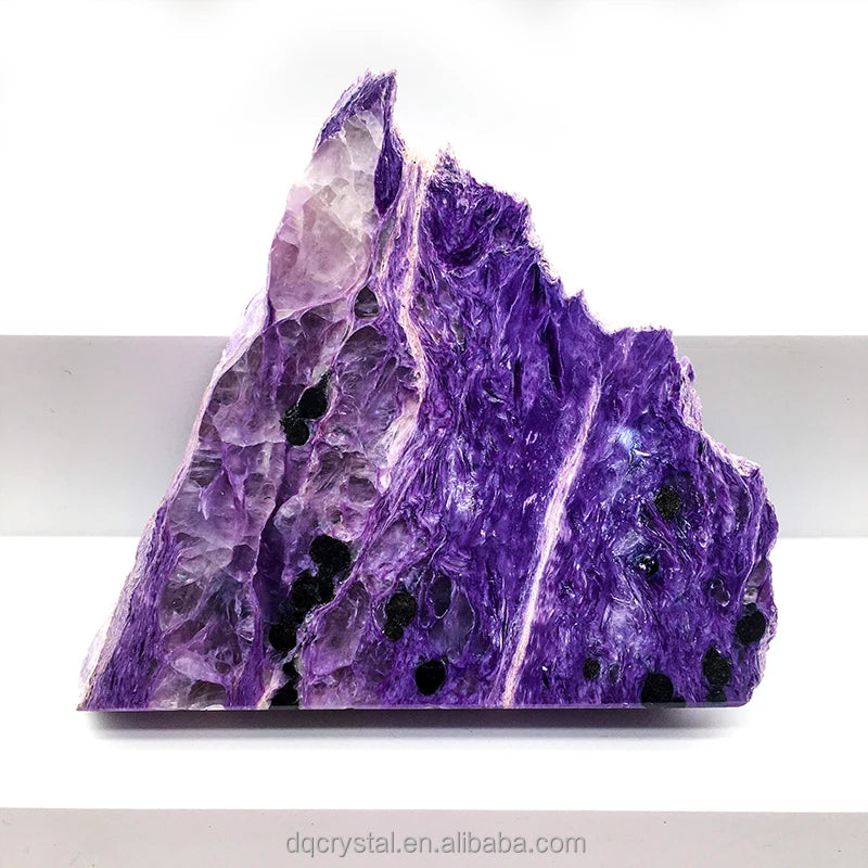 Polished purple charoite slice stone with dark pore-like spots, rugged mountain shape
