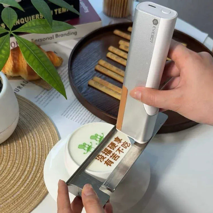 Handheld white coffee printer pen with display screen, printing over a plate