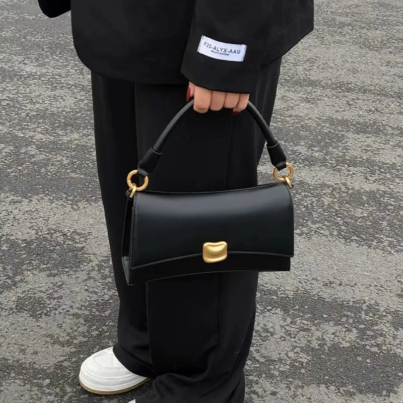 Black luxury designer handbag in square PU leather with gold magnetic clasp, structured top handle, and refined finish.