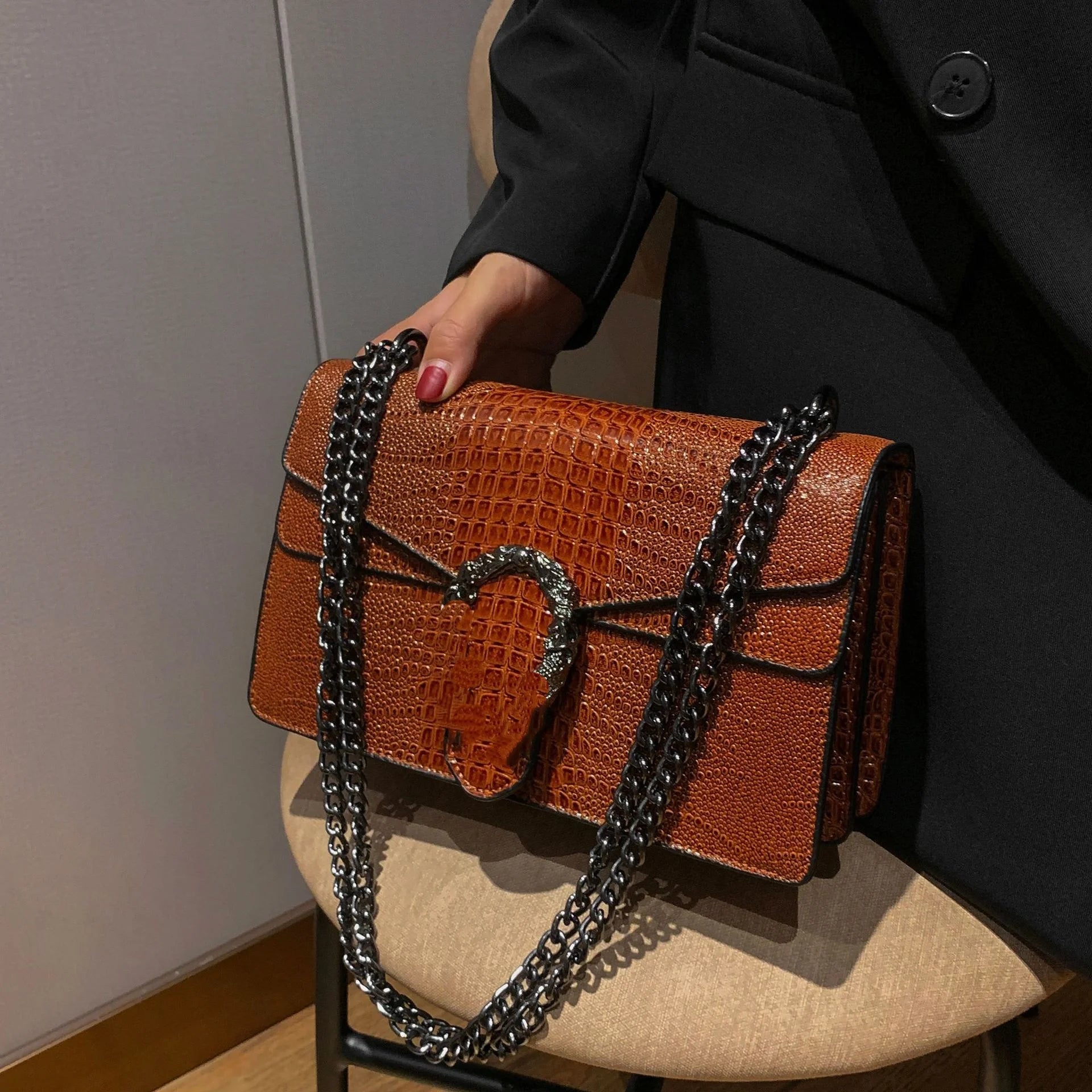 Brown crocodile-pattern crossbody trunk bag with dark metallic chain strap and horseshoe clasp hardware.