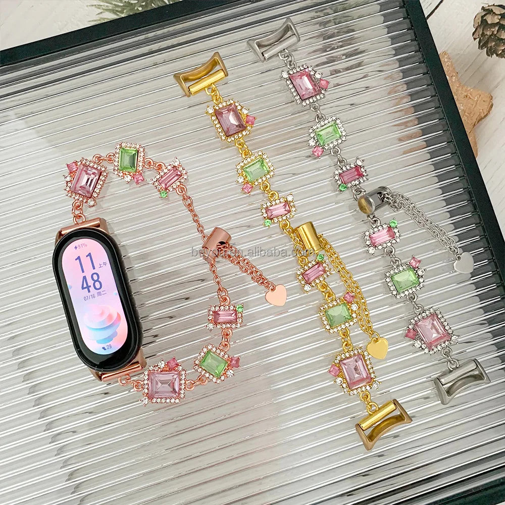Jewelry-style smartwatch bands with pink and green rectangular crystals in gold, silver, and rose gold metal chains.