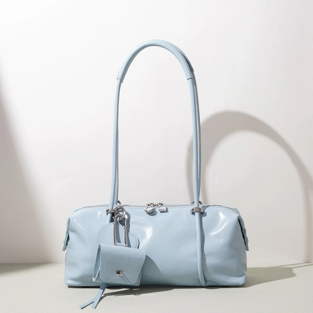 Light blue Boston shoulder bag with luxe glossy finish, minimalist pillow shape, zipper closure, and small charm pouch.