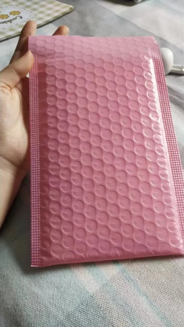 Pink padded bubble mailer envelope held in hand, opaque bubble texture
