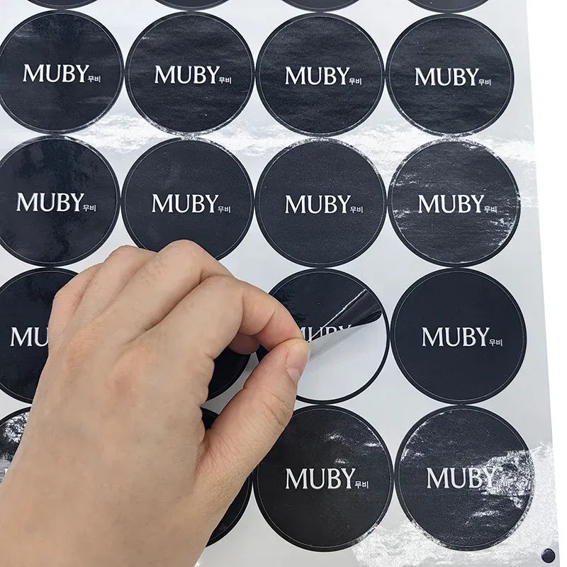 Round dark MUBY logo stickers on a sheet, adhesive circular labels