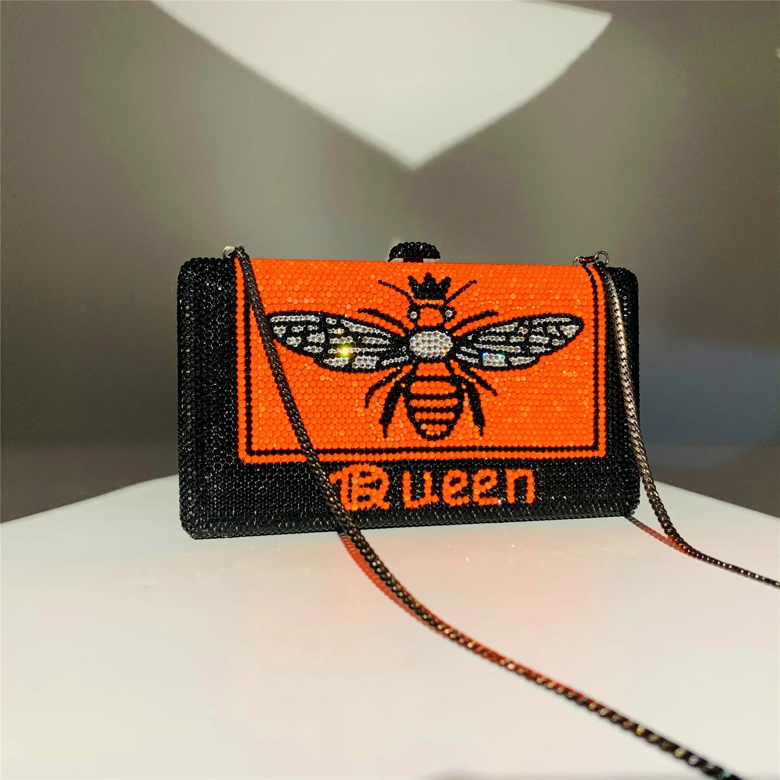 Black and orange rhinestone hard-shell evening clutch with Queen bee pattern and detachable chain strap.