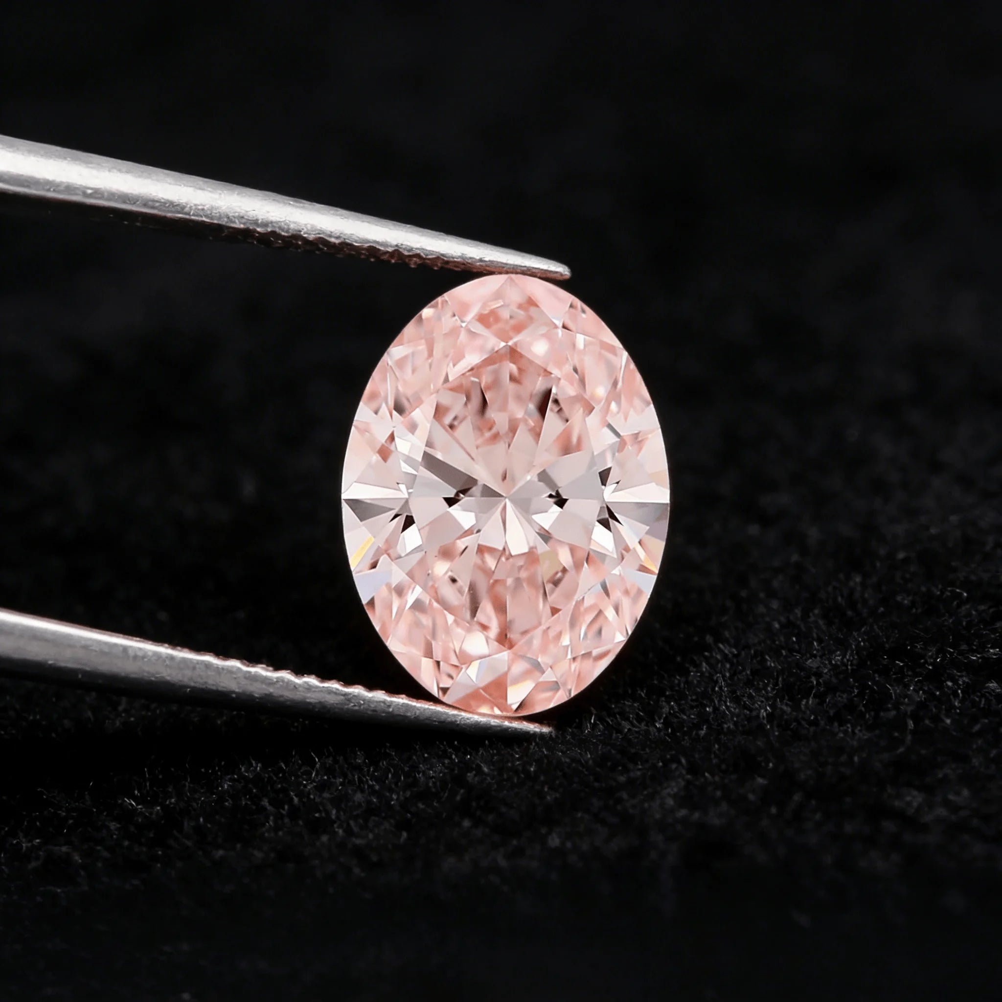 Oval fancy pink lab-grown diamond in tweezers with face-up sparkle
