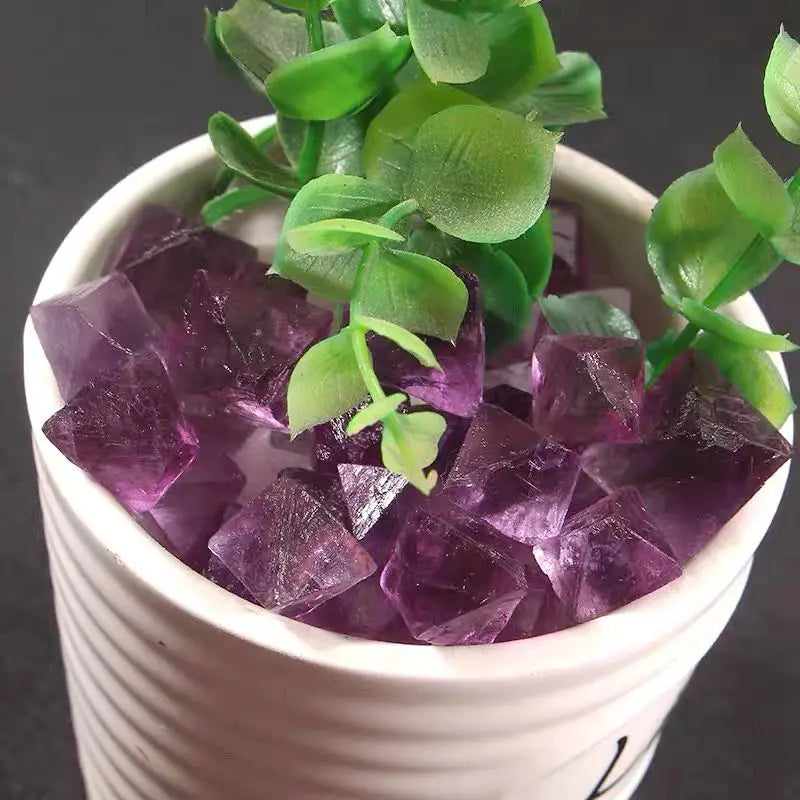 Purple rough crystal octahedra piled in white pot, faceted stones with glossy faces