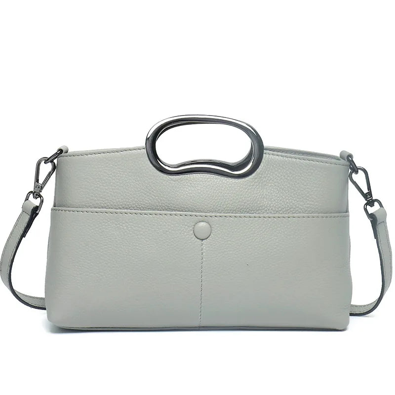 Grey designer crossbody bag in textured PU leather with unique metallic oval handle and detachable shoulder strap.
