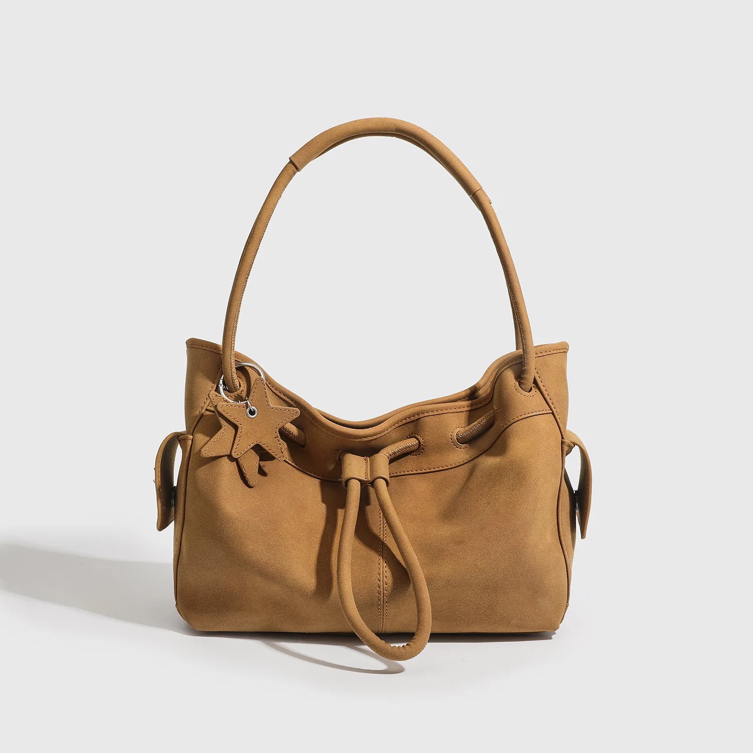 Tan suede designer shoulder bag with drawstring closure, star charm, and two straps for commuting or daily luxury.
