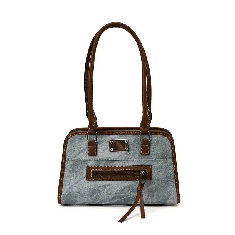 Large grey soft leather tote bag with brown trim, shoulder straps, front zipper pocket, and metal plaque detail.
