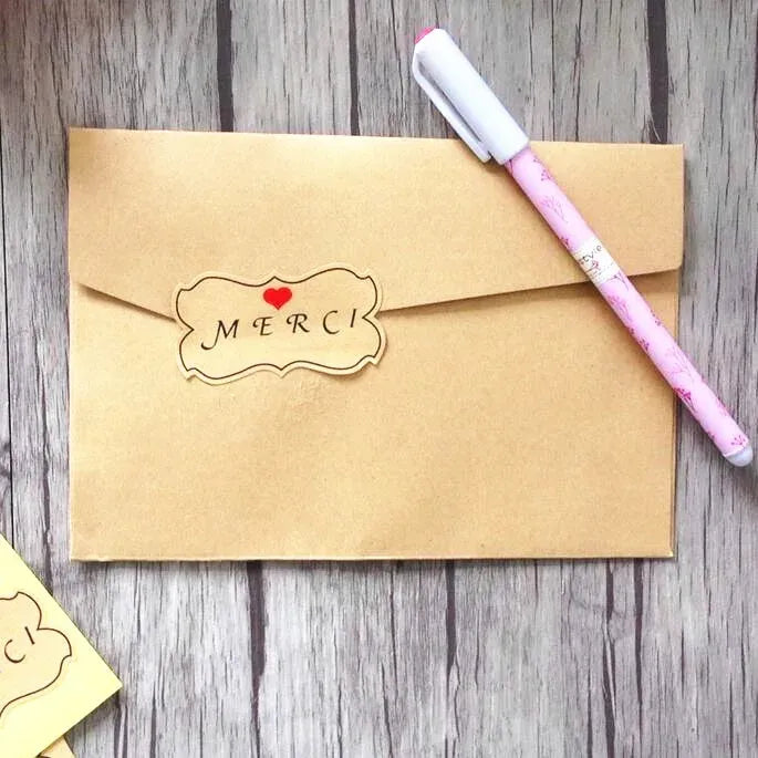 Kraft envelope with flower-shaped MERCI label sticker and red heart accent
