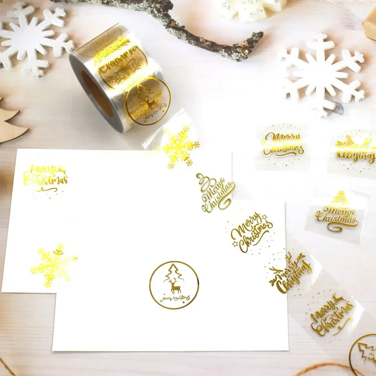 Round gold Christmas stickers on a transparent roll, featuring snowflakes, tree, and “Merry Christmas”.