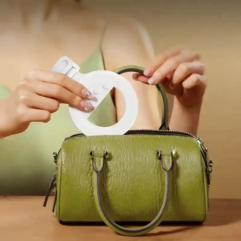 White portable circular LED ring light being placed into a small green textured handbag.