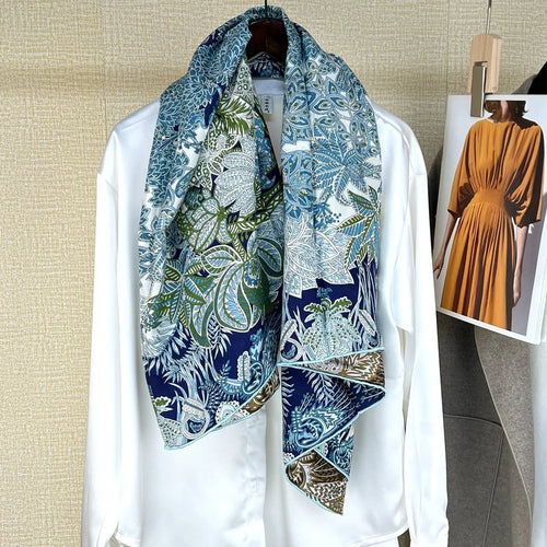 Luxury women’s square silk scarf featuring a blue, green, and white tropical botanical print pattern on a white blouse.