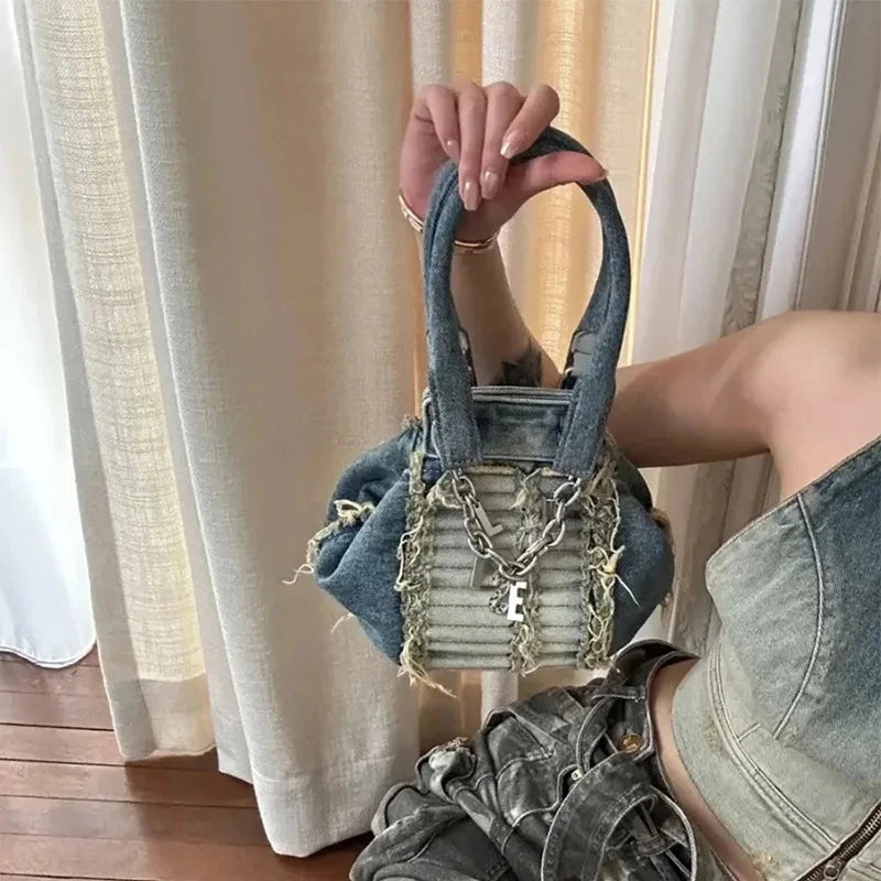 Small vintage-wash denim hobo bag with frayed edges, silver chain detail, and pleated front panel for women.