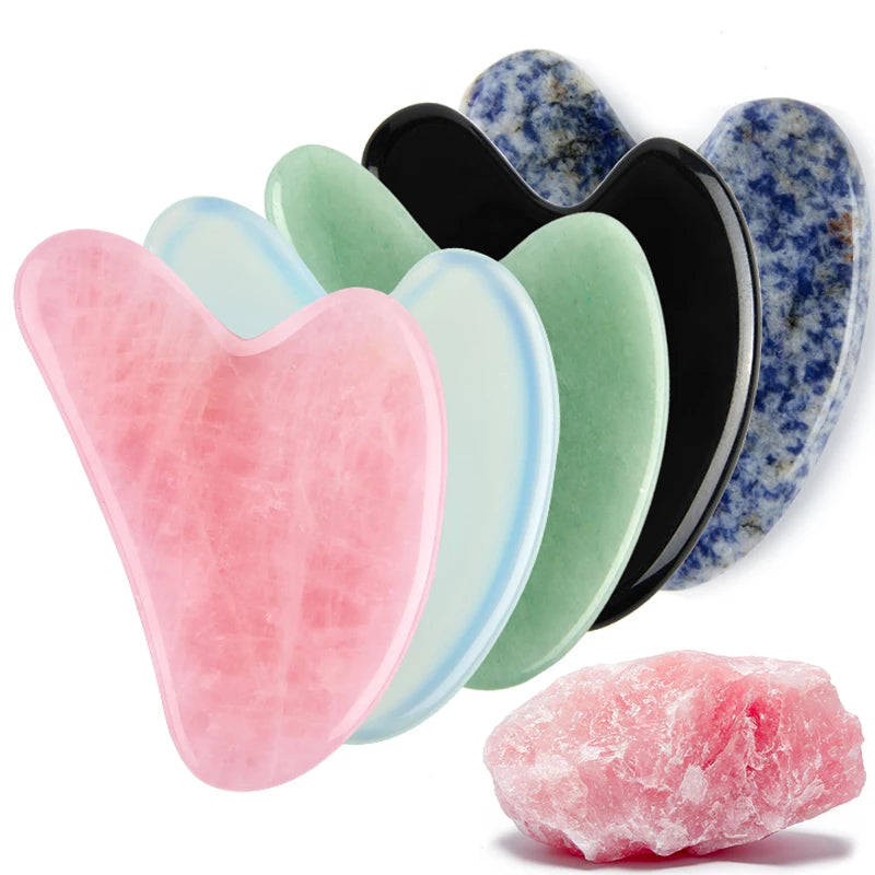 A collection of five heart-shaped gua sha stone facial massage tools in pink, white, green, black, and blue.