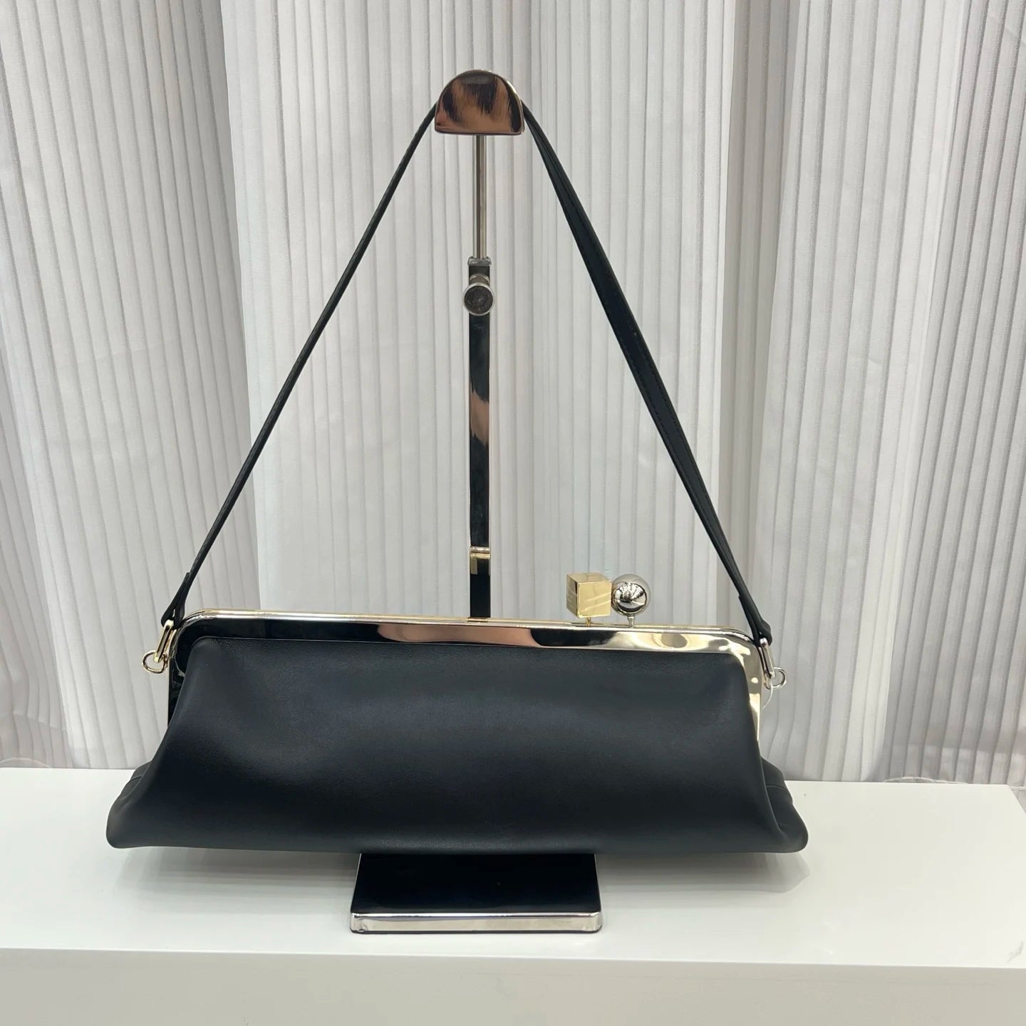 Black leather designer shoulder bag with a sleek metal frame, top clip closure, and minimalist structured silhouette.