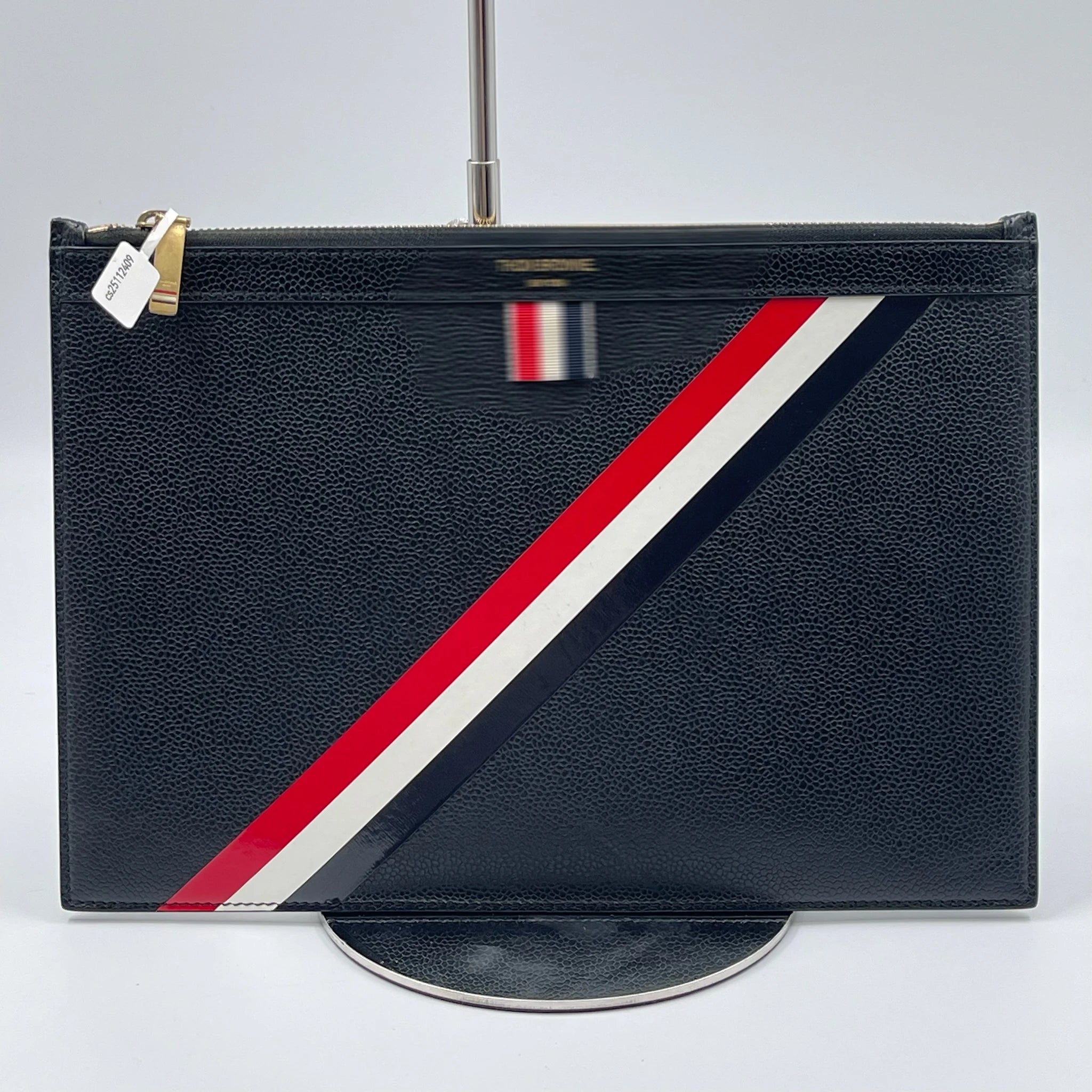 Black leather Thom Browne designer clutch with signature red, white, and blue diagonal stripe and gold zipper.