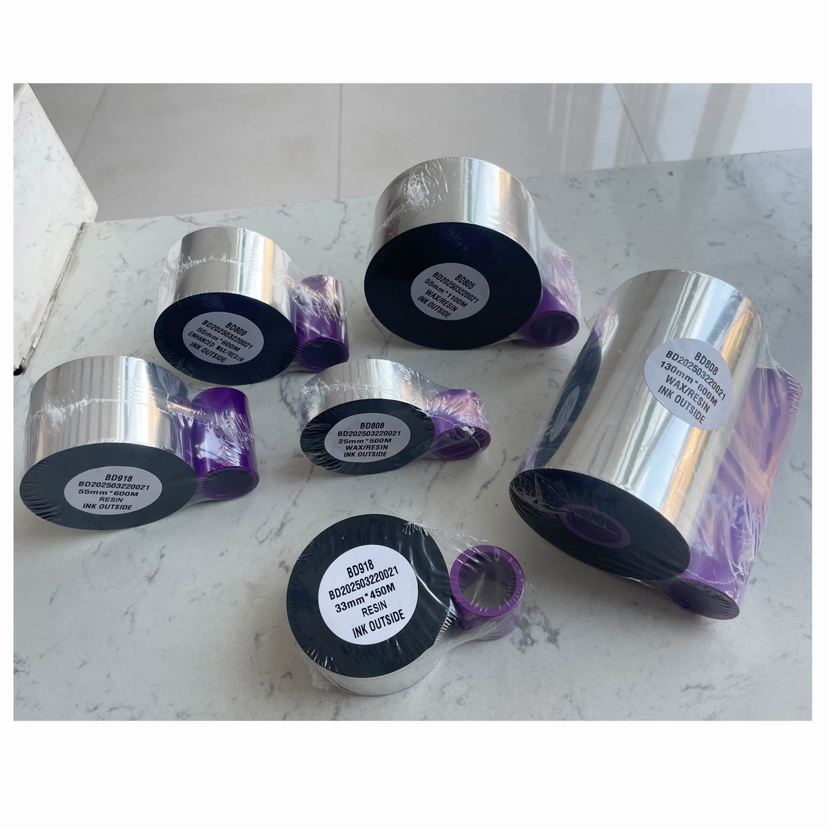 Multiple wax/resin ribbon rolls on a marble surface, silver outer and dark inner