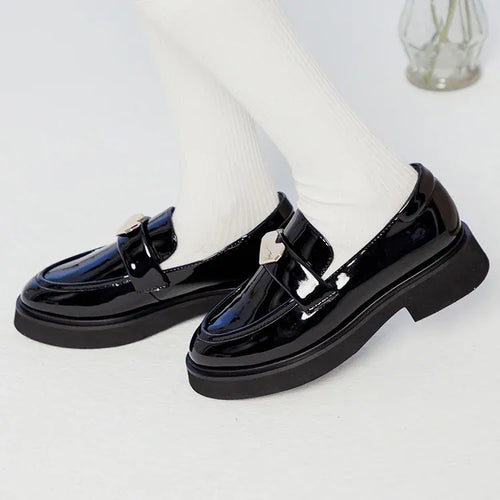 Black patent leather luxury loafers featuring a metallic heart charm and chunky platform sole.