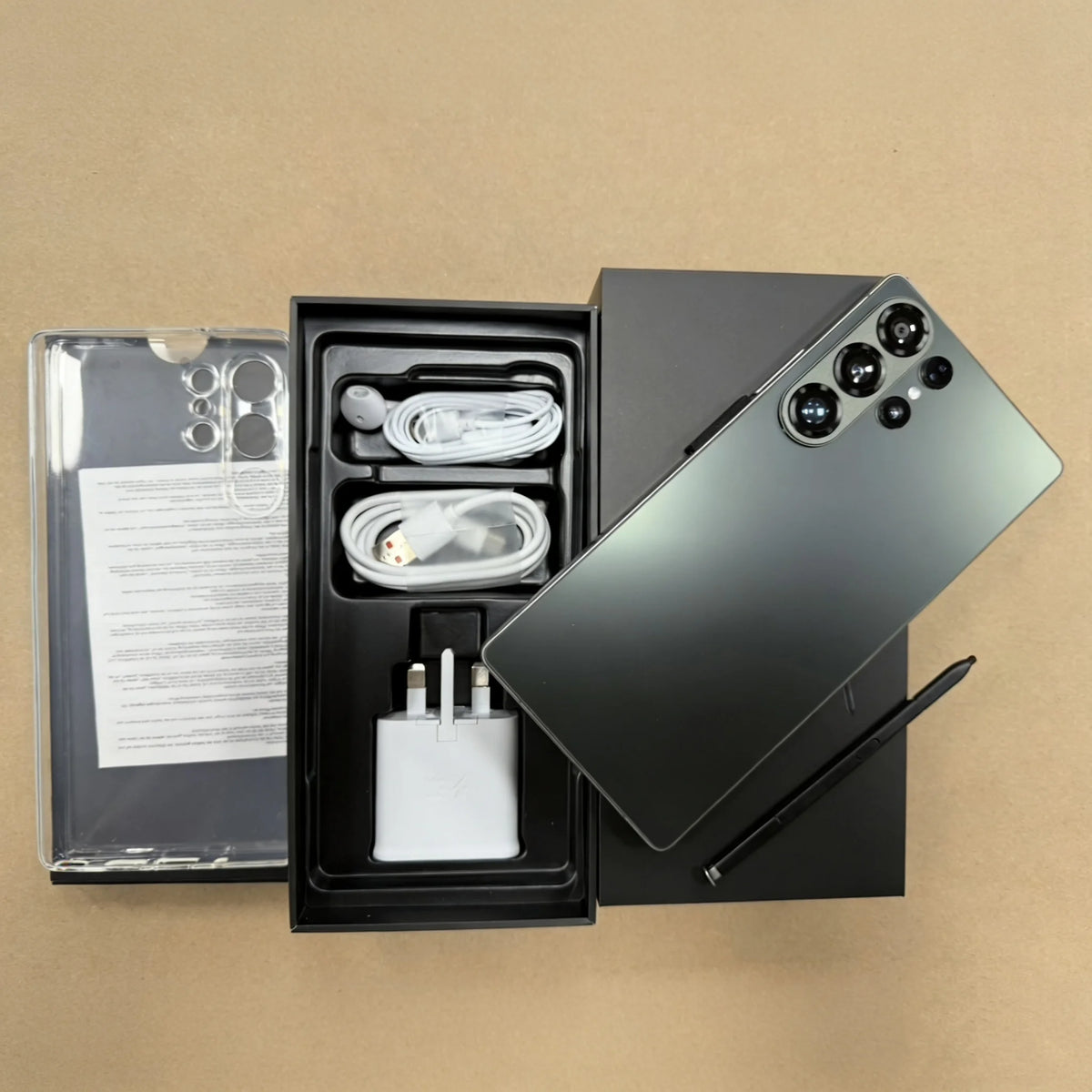 Unlocked smartphone in dark green with four rear cameras; open box with cables