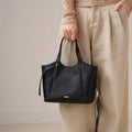 Black genuine top grain leather designer handbag with gold accents, retro tote style, held by hand.