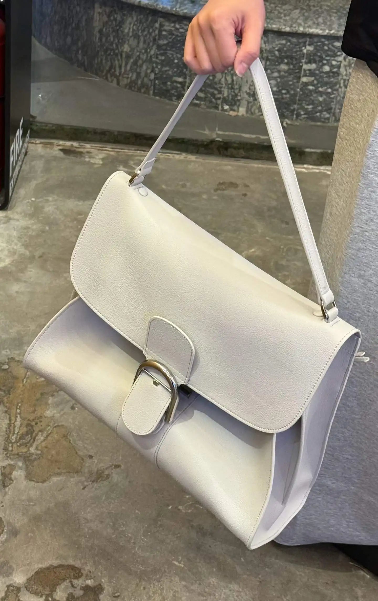 Off-white designer leather shoulder bag with a curved silhouette, structured flap, and gold buckle closure.