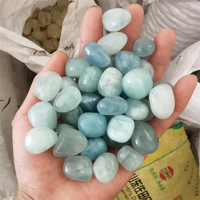 Clump of tumbled sky-blue aquamarine crystals on open palm, smooth rounded stones