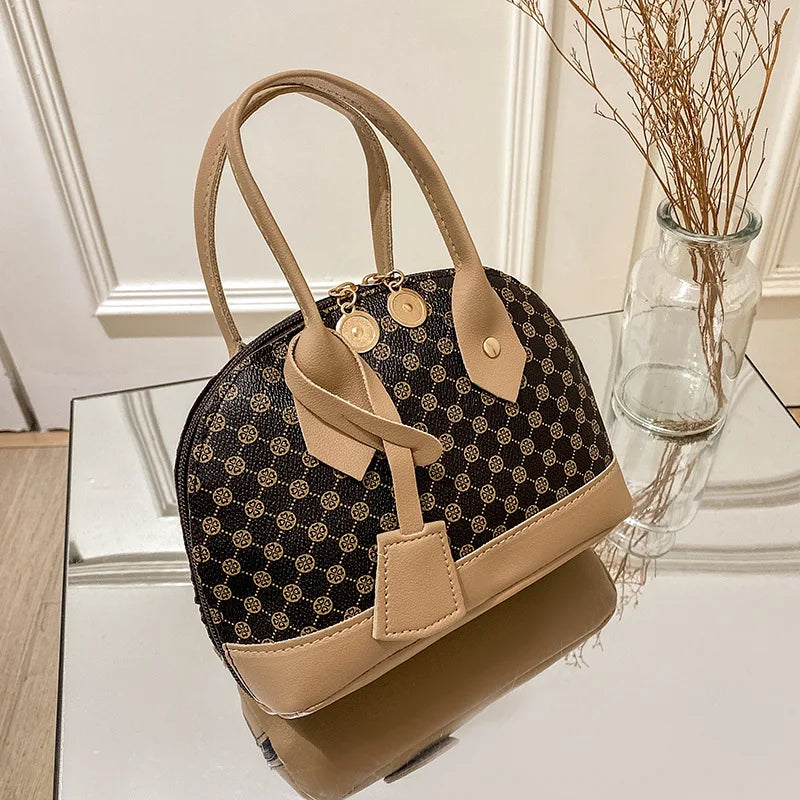 Brown designer shell handbag with beige trim, patterned print, dual top handles, and metallic zipper pulls.