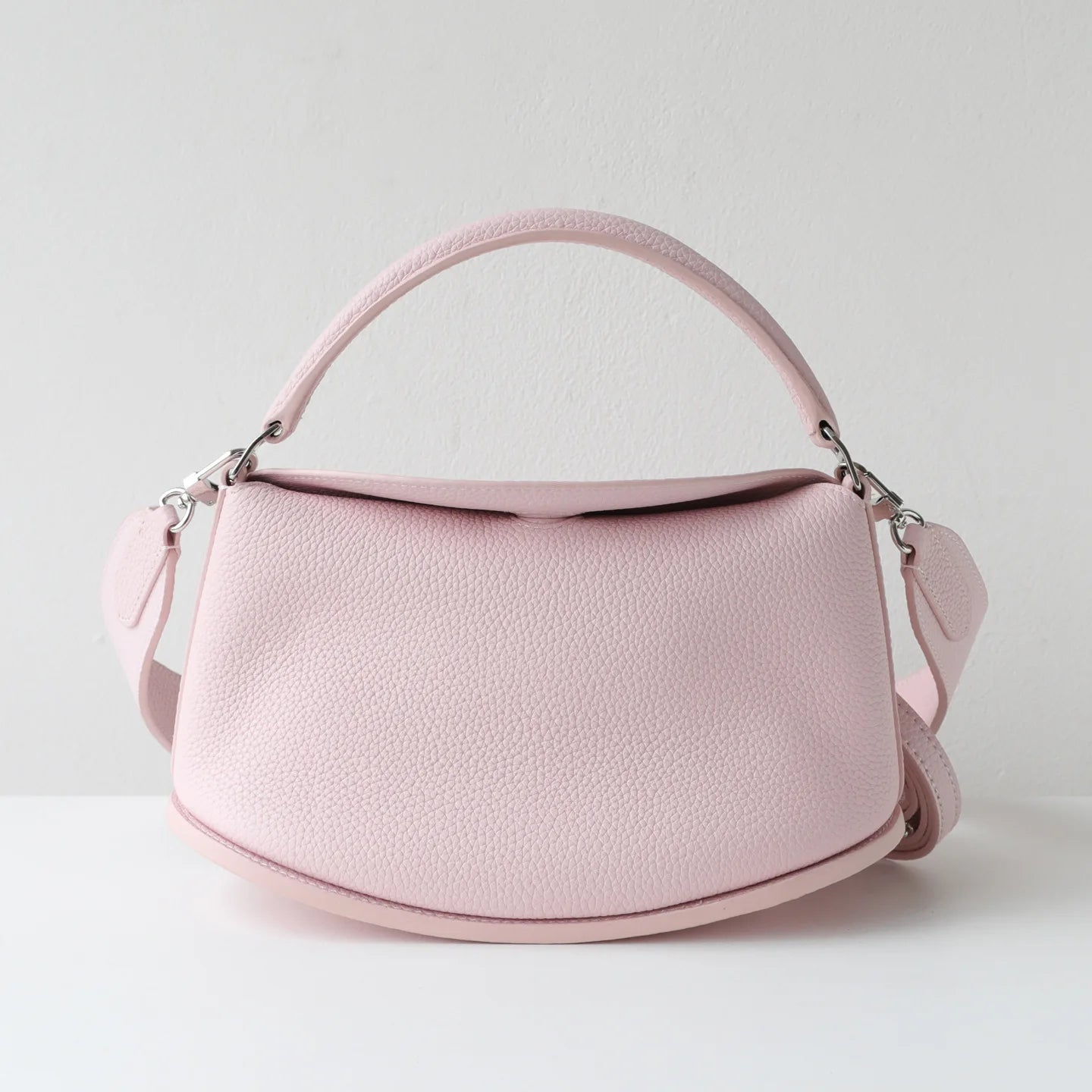 Pink top-layer cowhide leather designer handbag, pillow-shaped with dual straps and a secure magnetic closure.