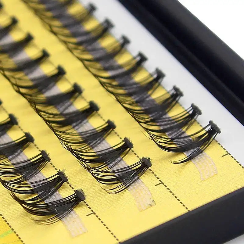 Close-up of black 20D Russian volume eyelash clusters arranged in neat rows on a yellow backing strip in a case.