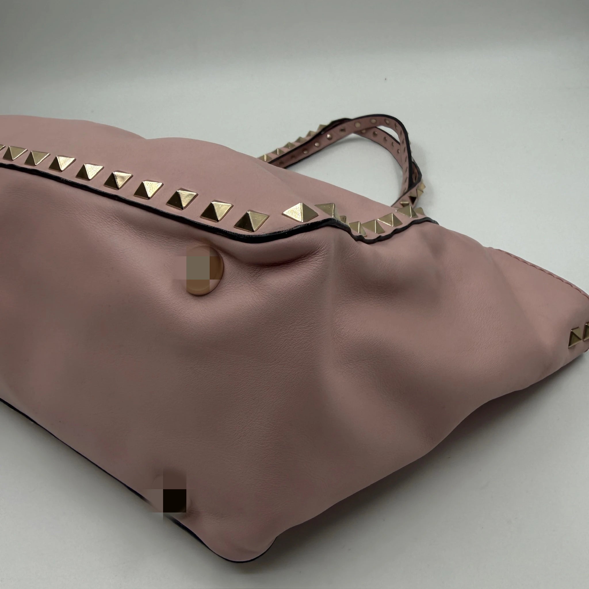 Pale pink genuine leather designer shoulder bag featuring gold pyramid rivet accents and a slouchy silhouette.