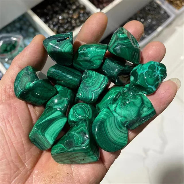 Assorted green malachite tumbled stones with marbled swirls held in hand