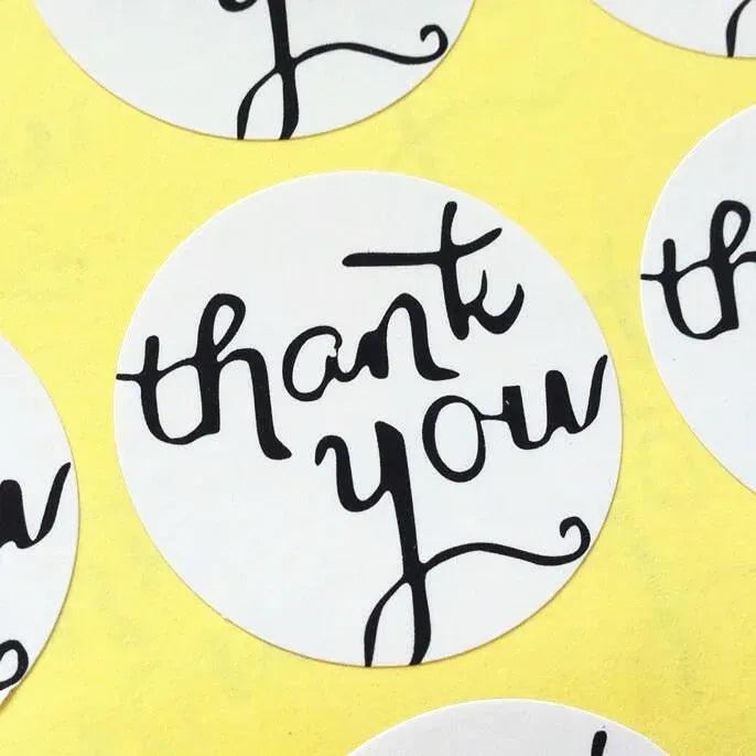 Close-up of a round white adhesive seal sticker with black “thank you” text.