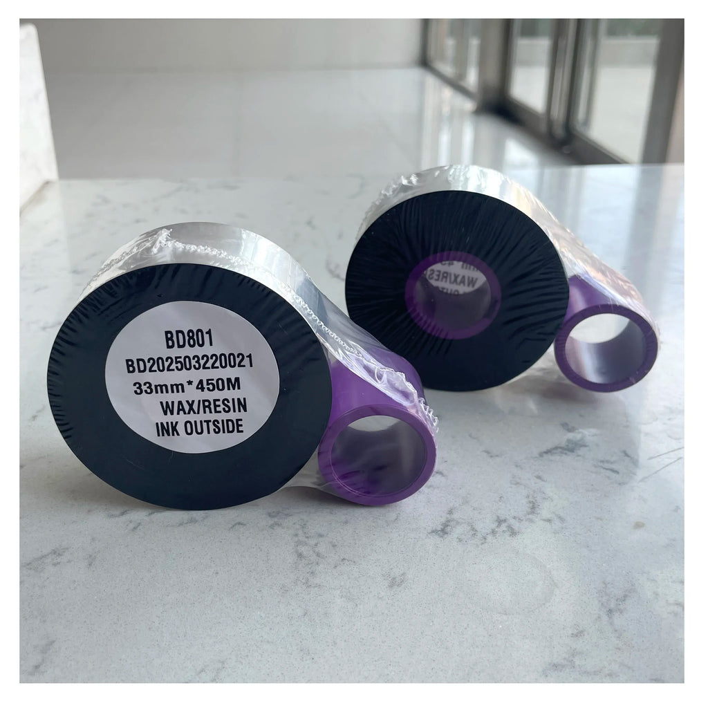 Thermal TTO ribbon rolls close-up, silver spools with black ink ribbon centers.