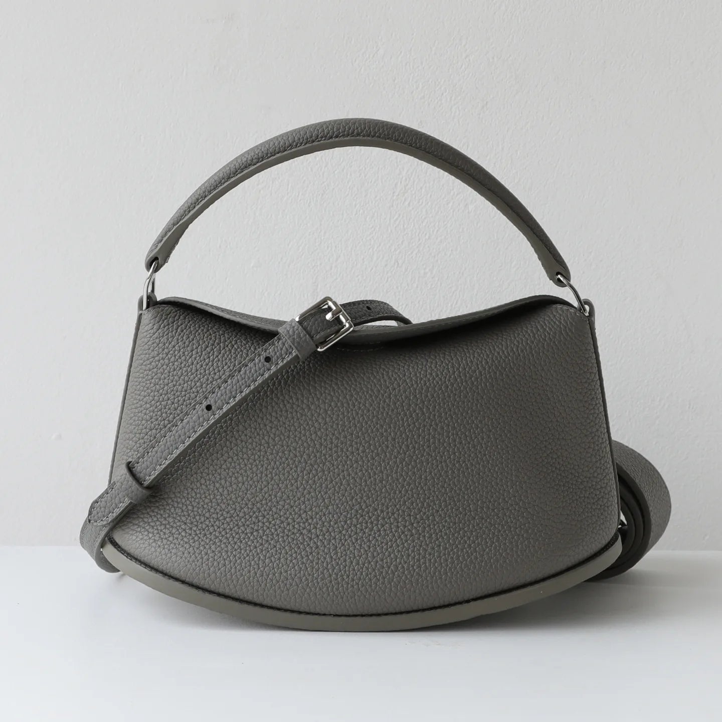 Elegant grey pebbled cowhide leather handbag, designer pillow-shaped commuting bag with top handle and buckle strap.