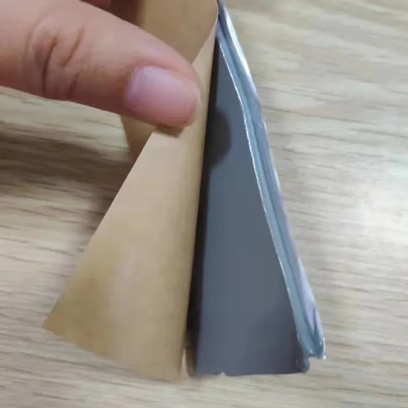 Gray waterproof tape strip with foil surface and liner, held between fingers
