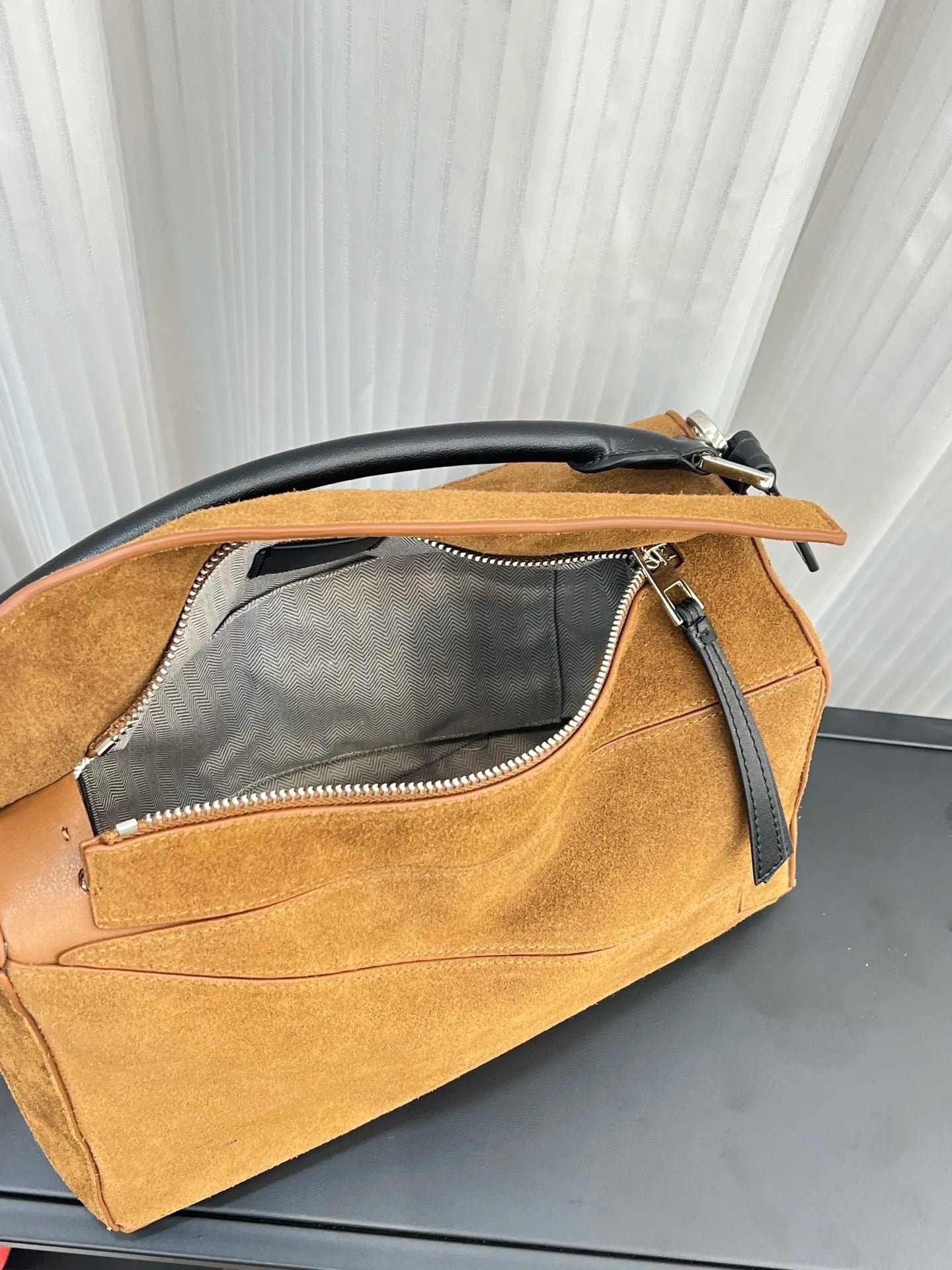 Tan suede designer handbag with black leather handle, zippered opening, and patterned interior lining.