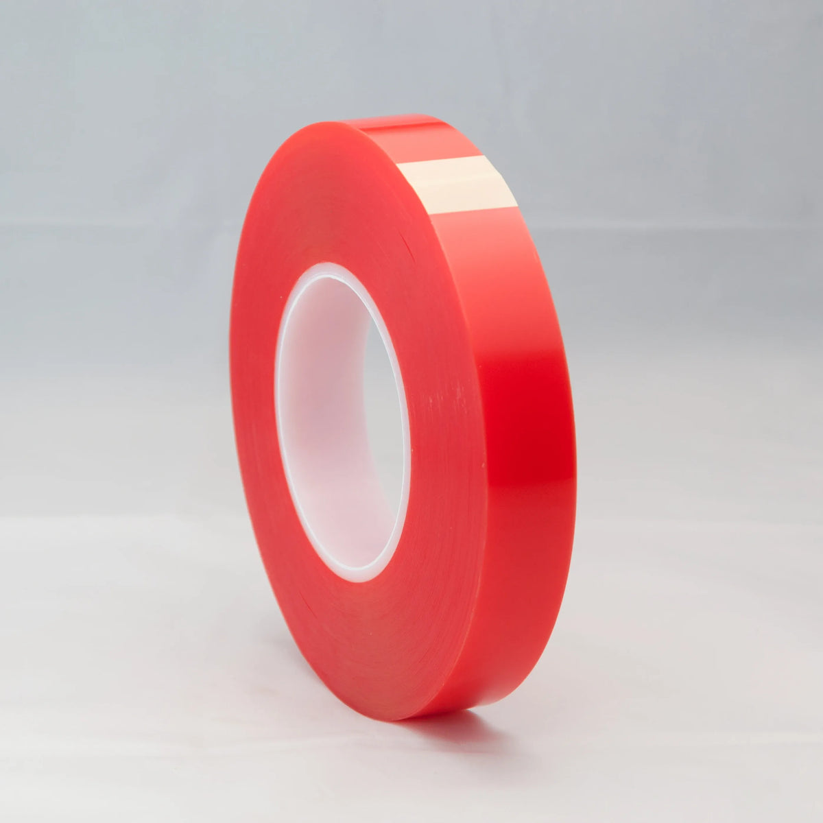 Red double-sided adhesive tape roll standing upright with white inner liner