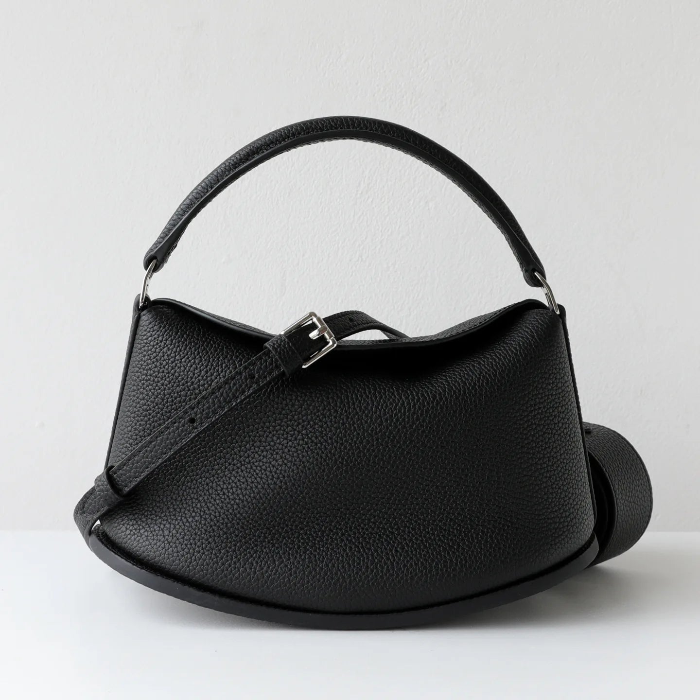 Elegant black pebbled cowhide leather handbag with pillow silhouette, dual straps, and adjustable buckle detail.