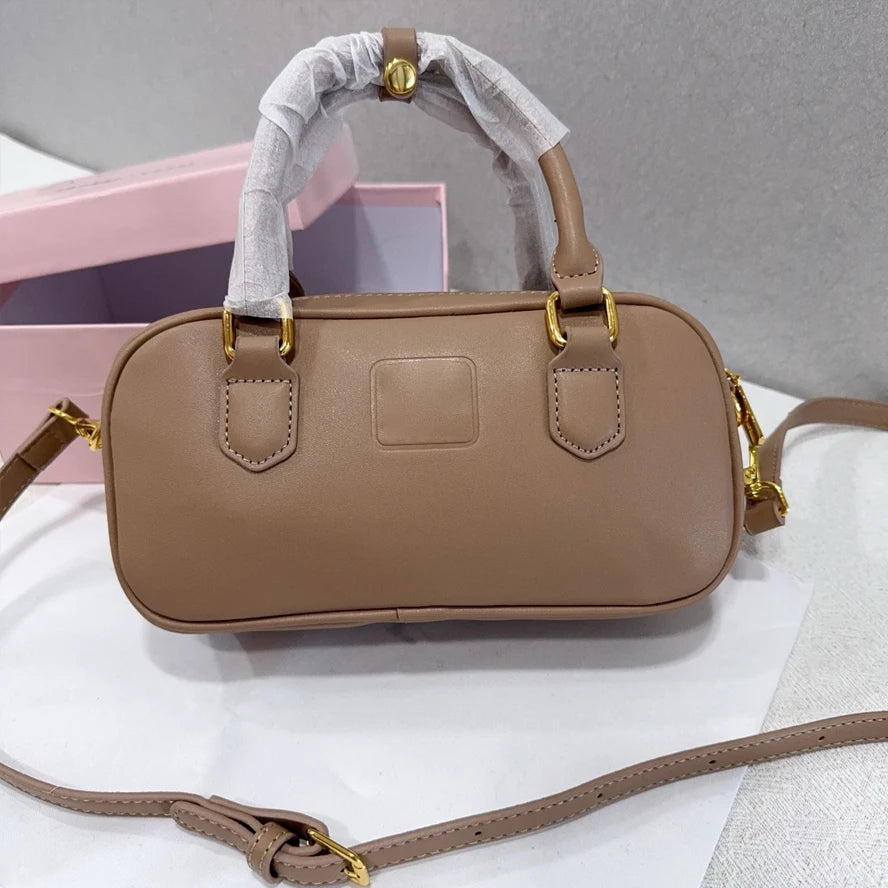 Taupe luxury leather trunk handbag with gold hardware, top handle, and adjustable shoulder strap.