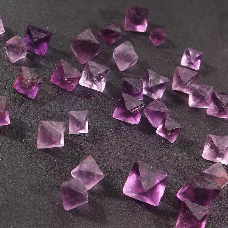 Purple fluorite crystal rough cubes and octahedrons scattered on dark surface