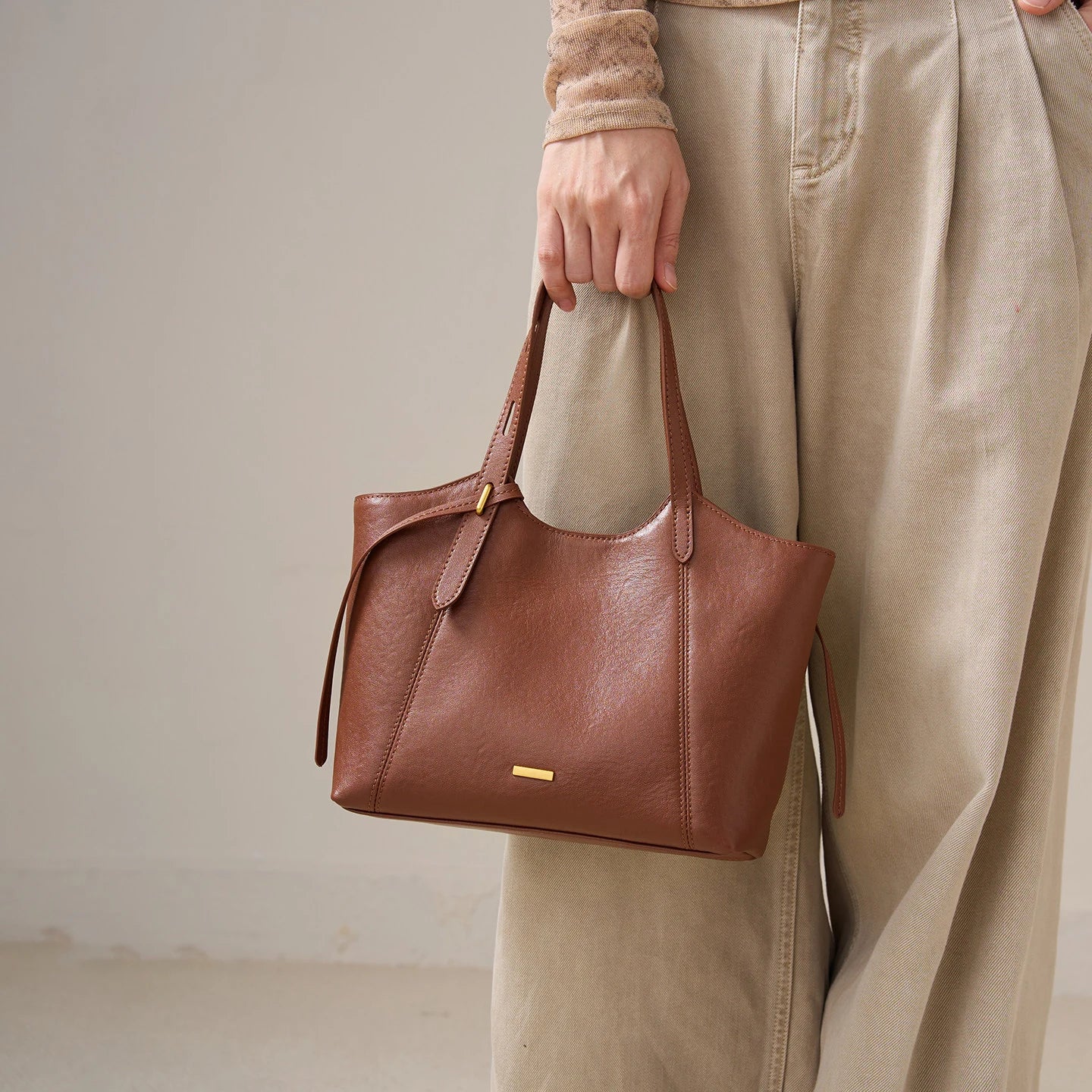 Brown top-grain leather designer handbag with a retro bucket silhouette, slim shoulder straps, and gold hardware.