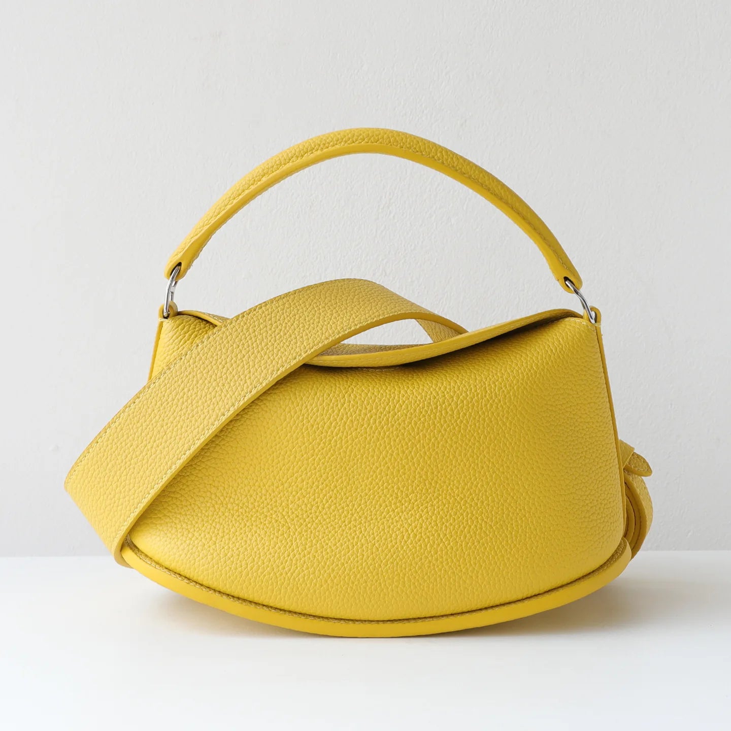 Yellow pebble-grain cowhide leather designer handbag, pillow-shaped with dual straps and magnetic closure.